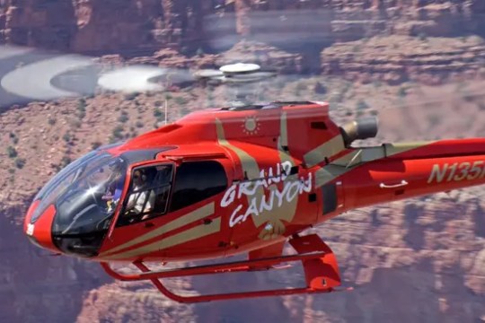 Red helicopter flying over Grand Canyon with 'Grand Canyon' text on side.