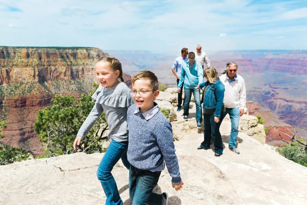 Group of people walking on a rocky path near a canyon under a clear blue sky.