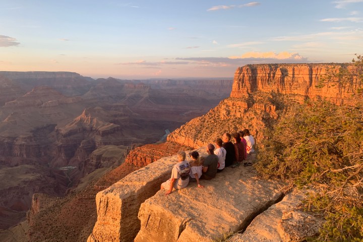 Group of people sitting on a cliff overlooking the Grand Canyon at sunset.