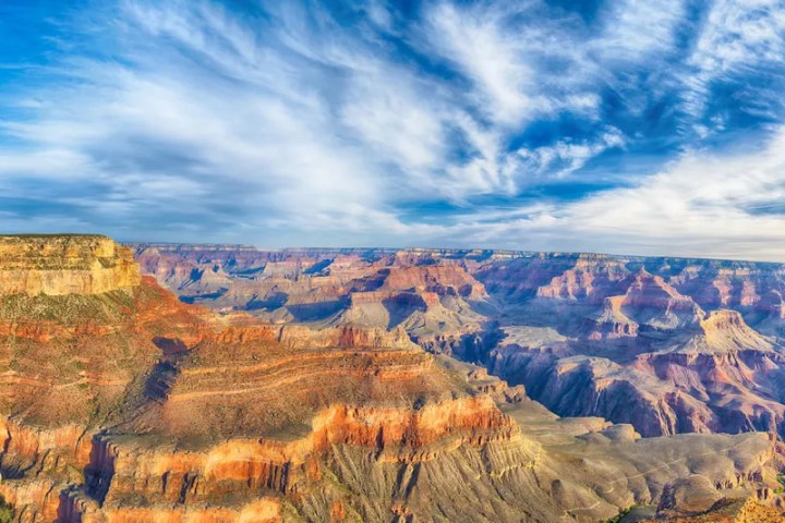 Grand Canyon with colorful layers and a cloudy blue sky.