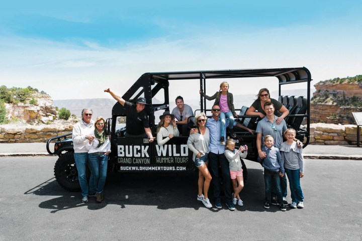 People posing with an off-road tour vehicle at a scenic overlook.