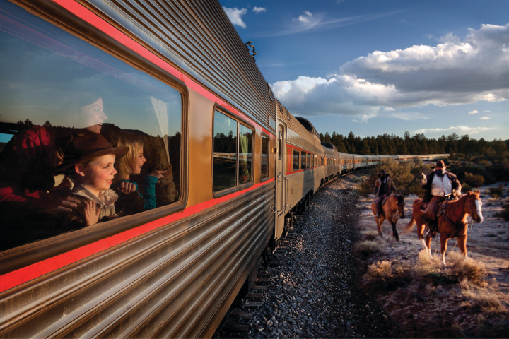 Children in a train watch cowboys on horses outside.