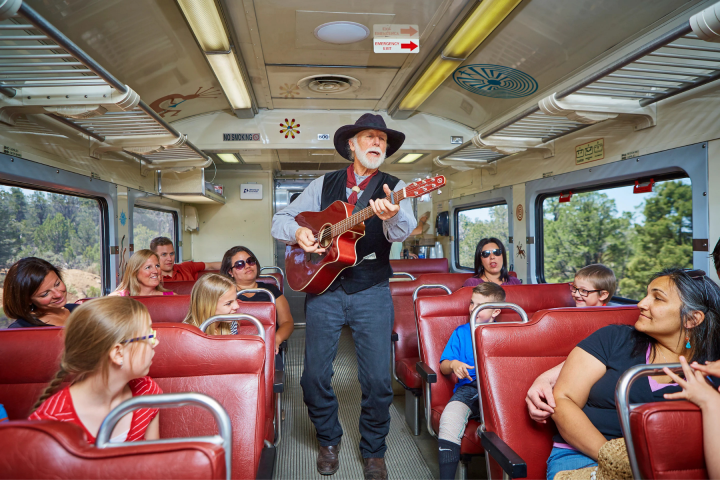 Man playing guitar on train, passengers smiling and listening.